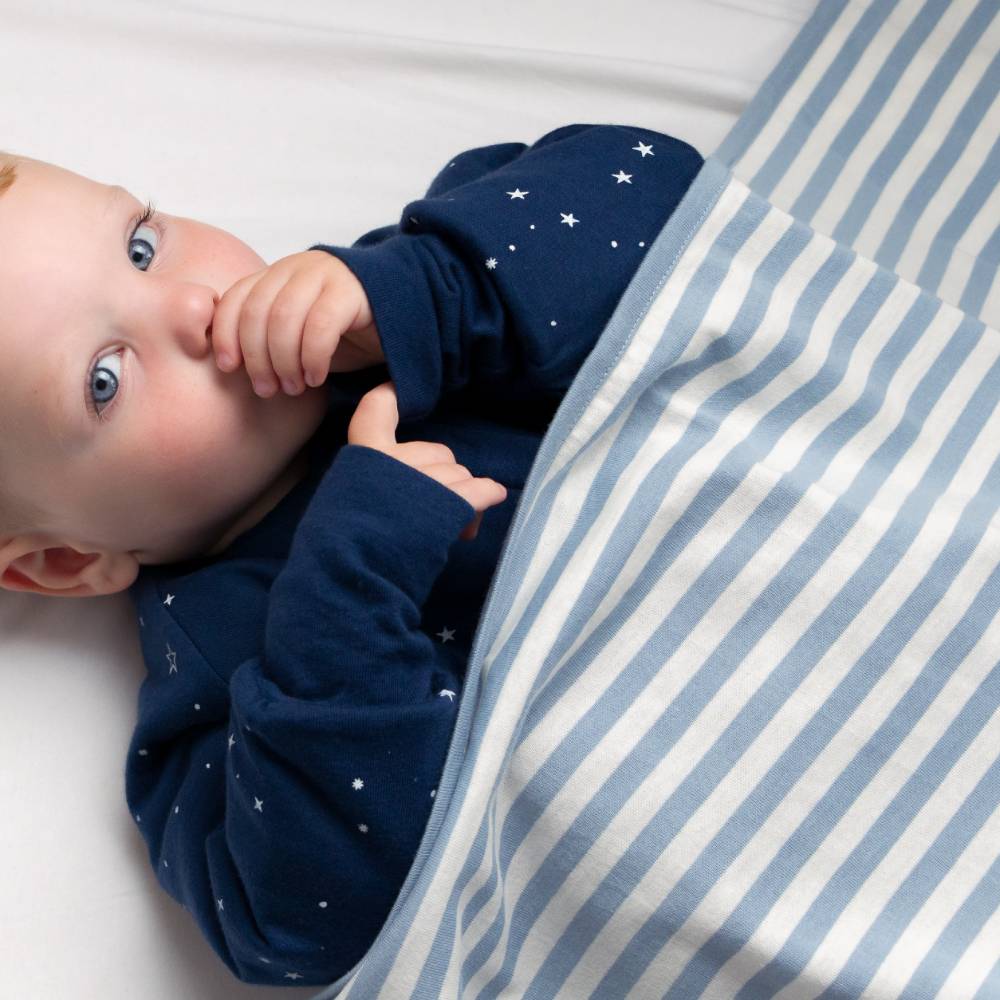 Baby in a navy blue outfit with star patterns lying on a white and blue striped blanket.