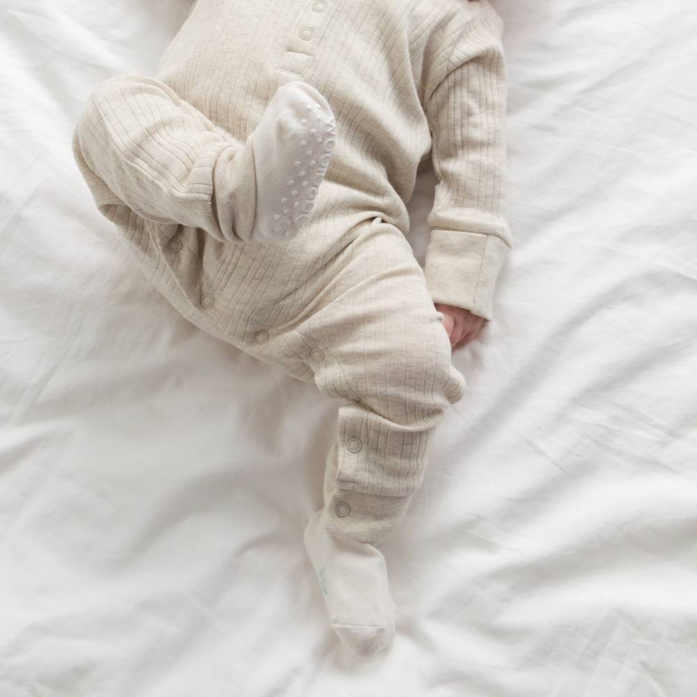 Baby in a beige onesie lying on a white bed