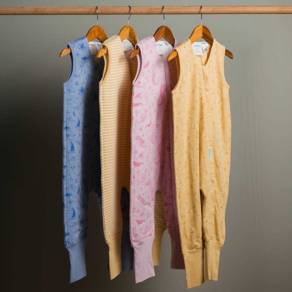 Four children's sleeveless rompers of different colors hanging on a rack against a gray background.
