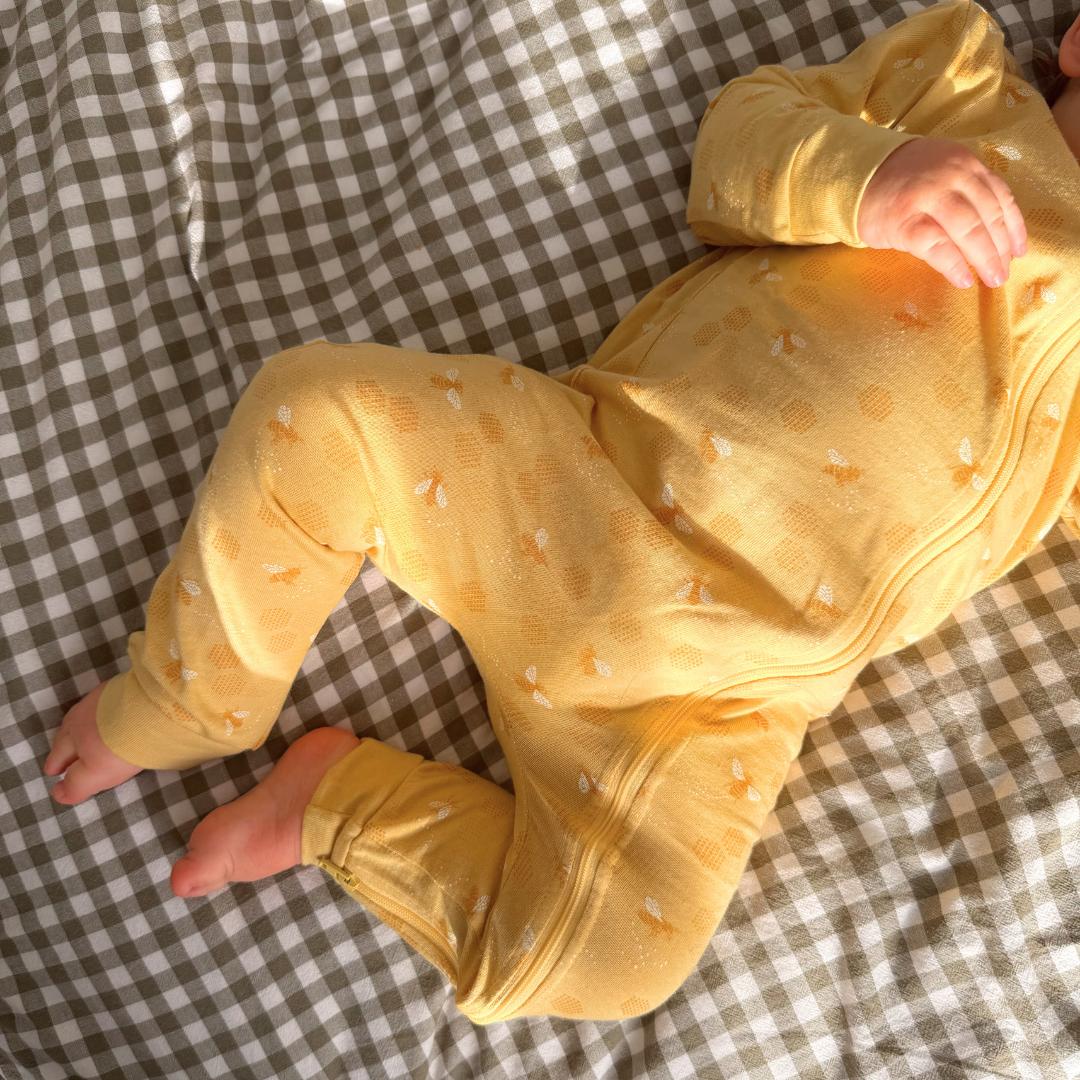 Baby in a yellow outfit with small patterns lying on a checkered blanket