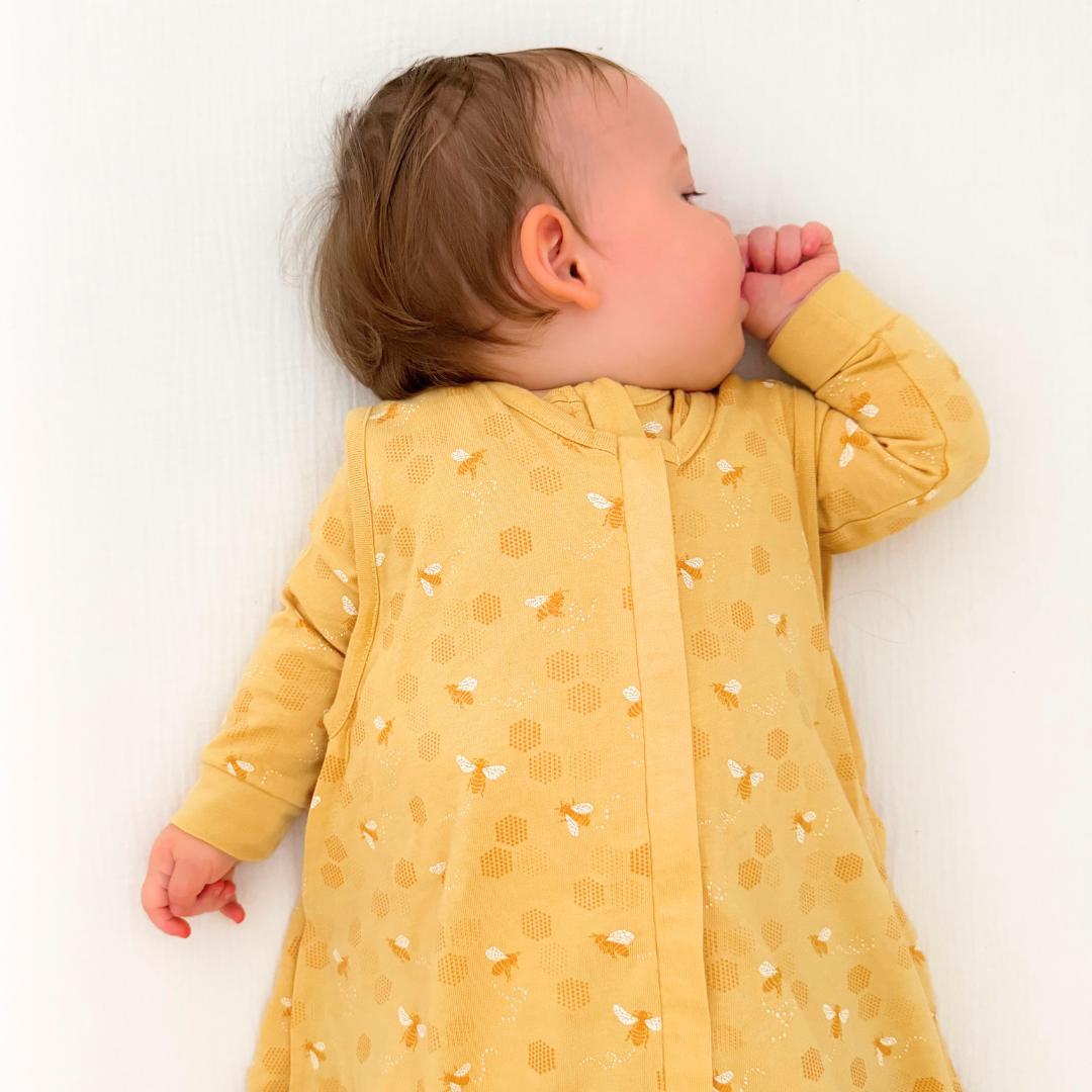 Baby wearing a yellow outfit with a yellow bee pattern, lying on a white background