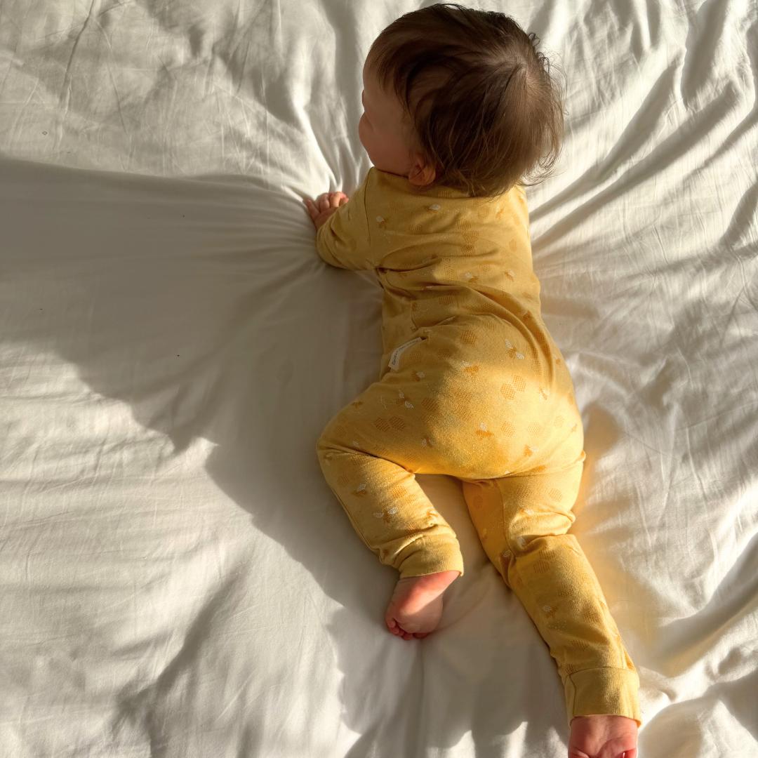 Baby in a yellow outfit lying on a white sheet