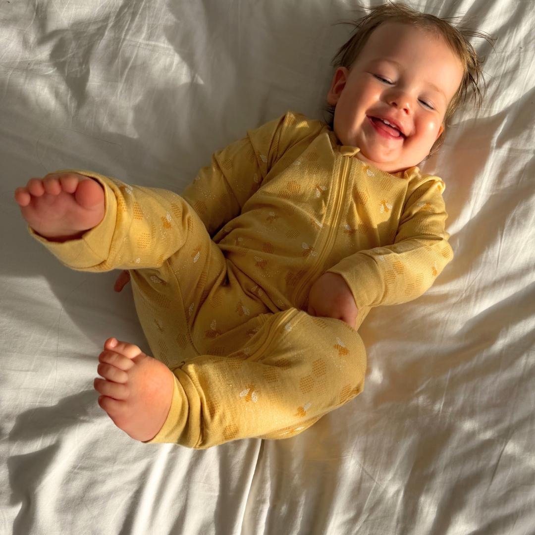 Child wearing a yellow onesie with a pattern, lying on a white surface.
