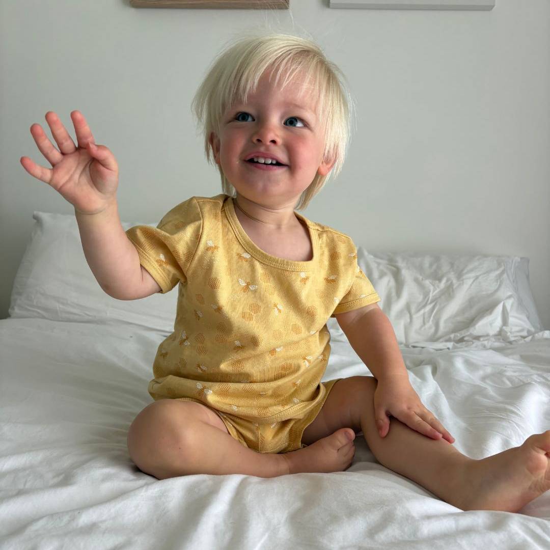 Child wearing woolbabe bee and yellow pyjamas  sitting on a bed