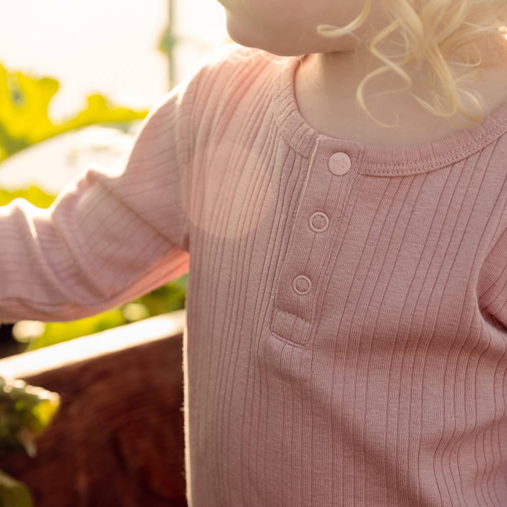 Close-up of a child wearing a pink ribbed long-sleeve shirt with buttons outdoors.