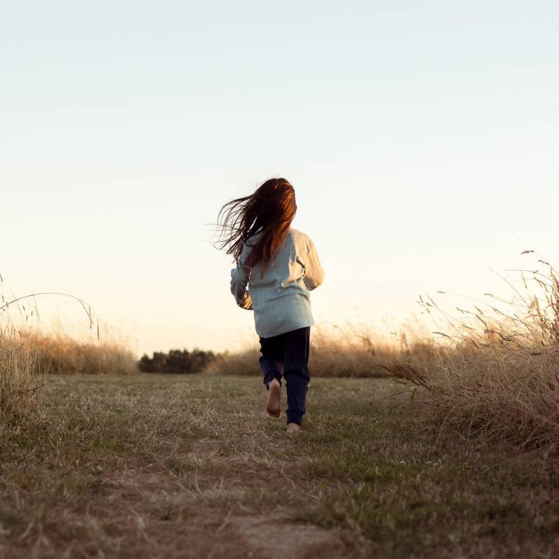 child running through a field at sunset