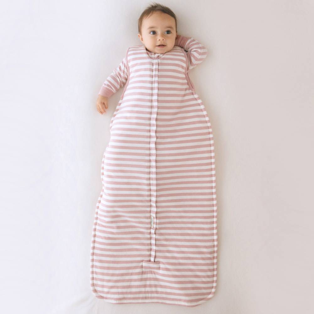 Baby lying on a white surface wearing a pink and white striped sleep sack