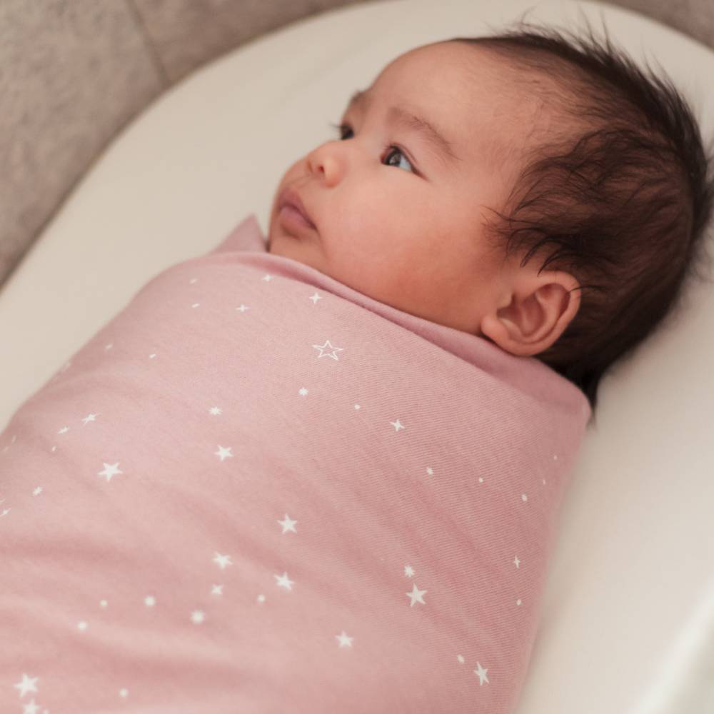 Newborn baby wrapped in a pink blanket with star patterns, lying on a white surface.