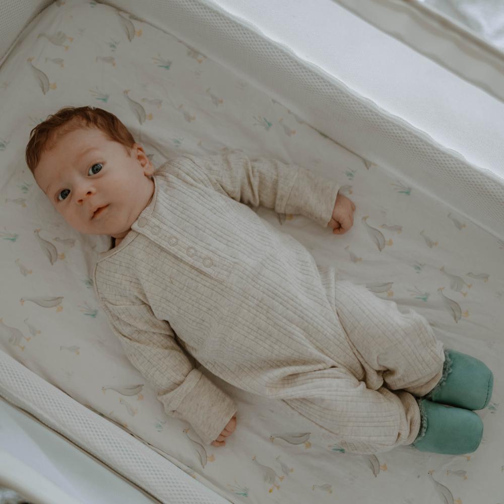Baby lying in a crib wearing a beige outfit and green socks.