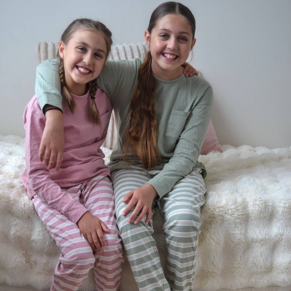 Two young girls in matching pajama sets sitting on a bed.