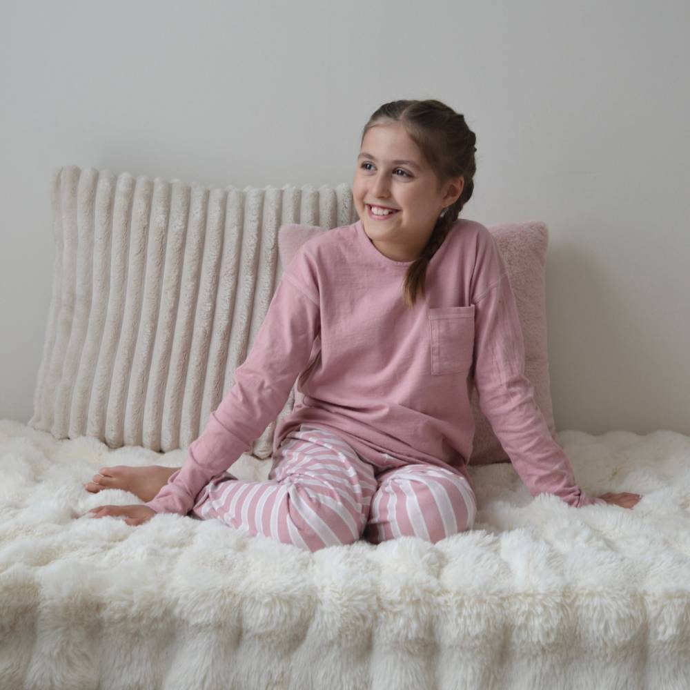 Young girl in pink pajamas sitting on a fluffy white bed with a neutral background