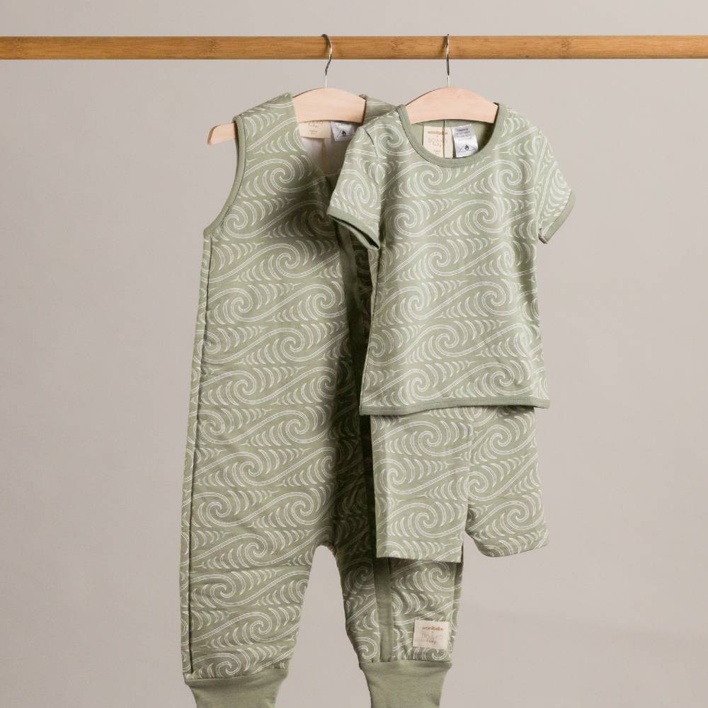 Children's green patterned outfit hanging on a wooden rack against a plain background