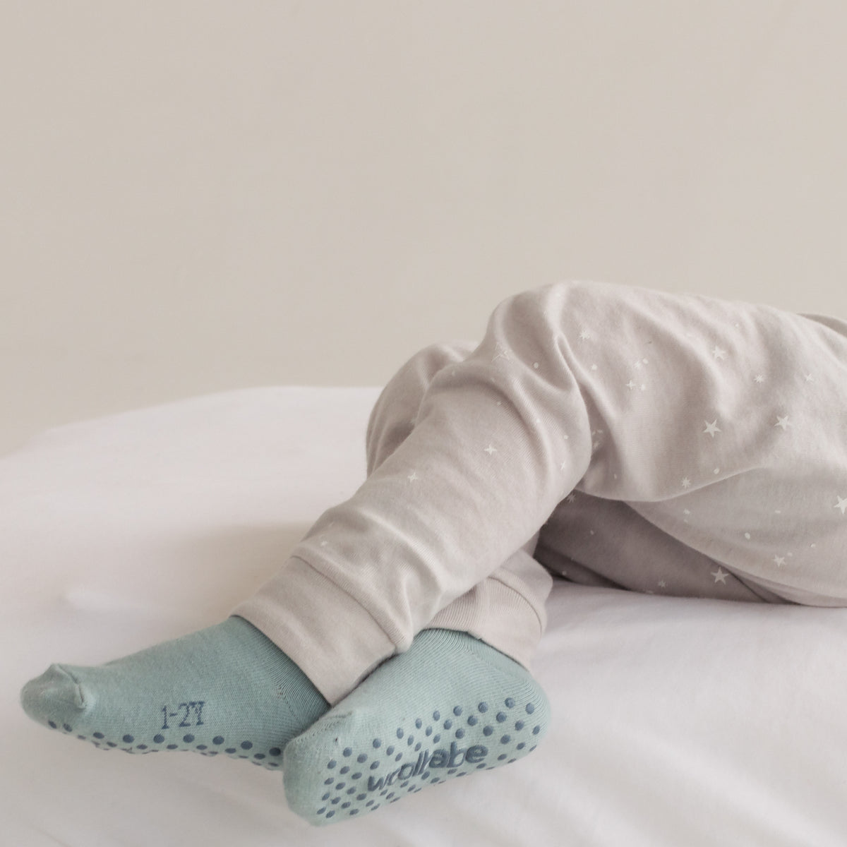 Baby legs wearing light gray pants and light blue socks on a white surface