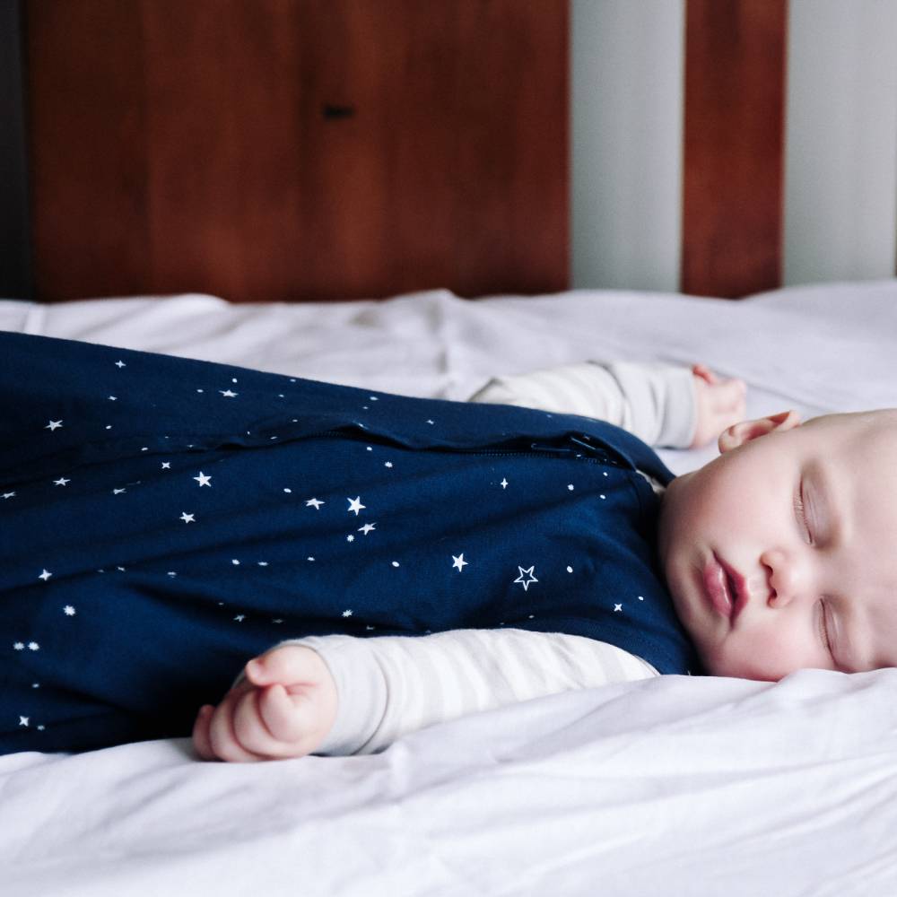 Baby sleeping on a bed wearing a navy blue outfit with white star patterns.