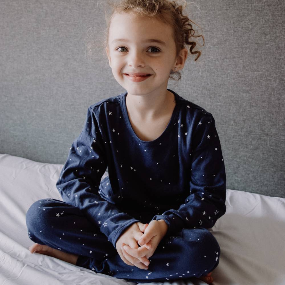 Child wearing navy blue pajamas with star patterns sitting on a bed.