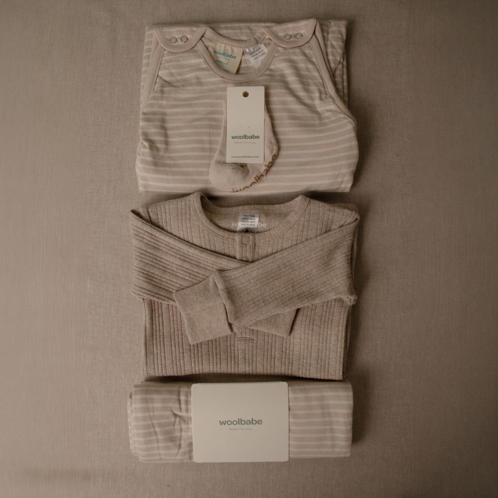 Folded baby clothing set with 'woolbabe' tags on a brown background