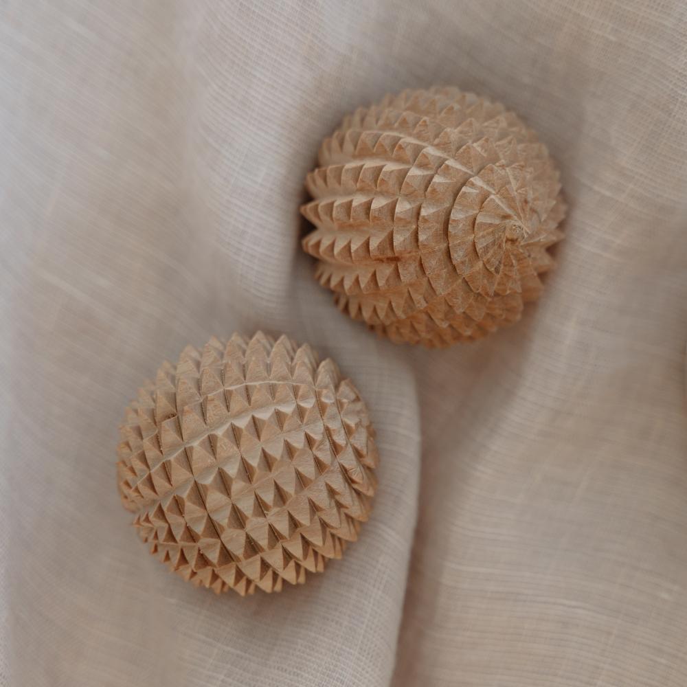 Two beige textured spikey massage balls on a beige fabric background