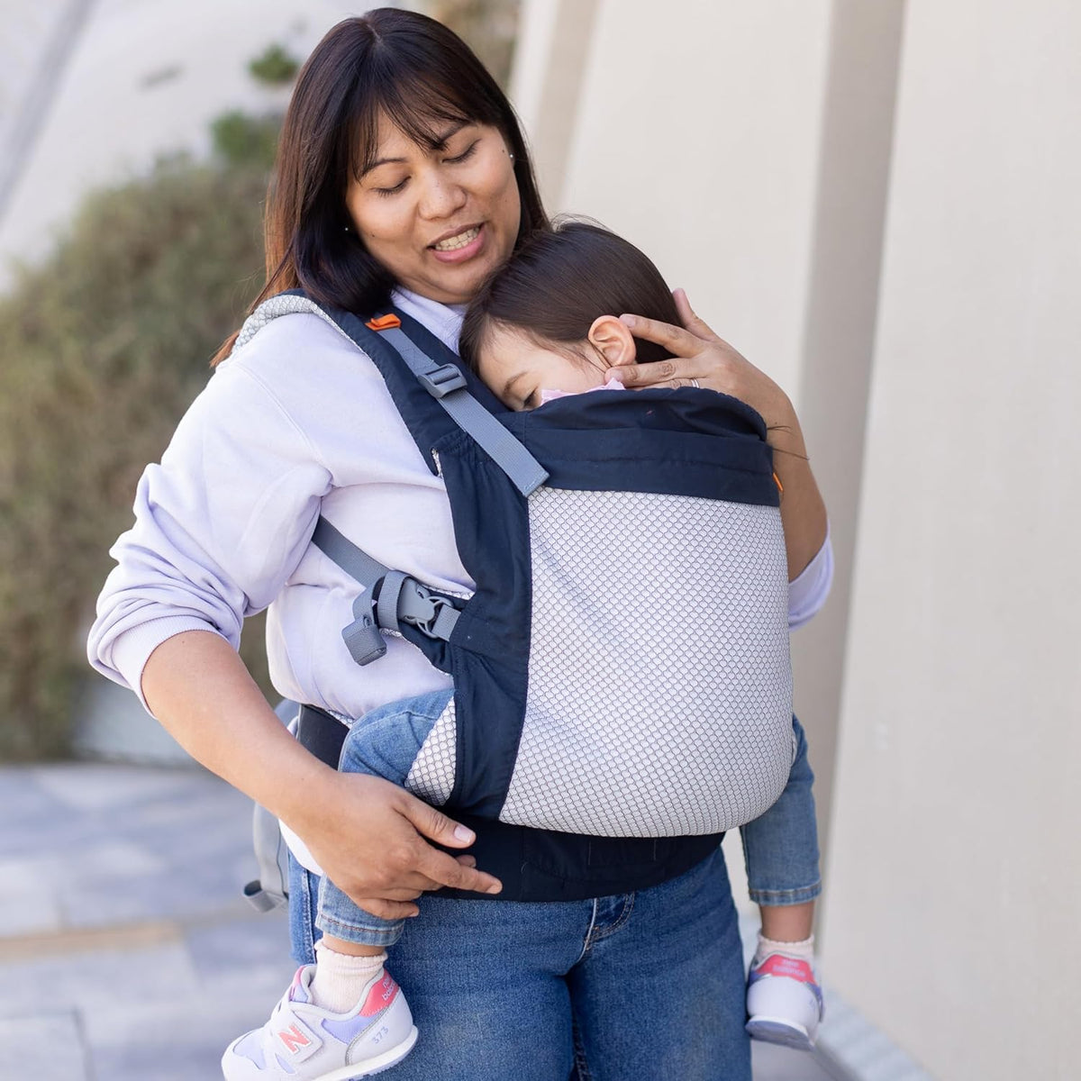 Woman holding an older child in a toddler carrier outdoors
