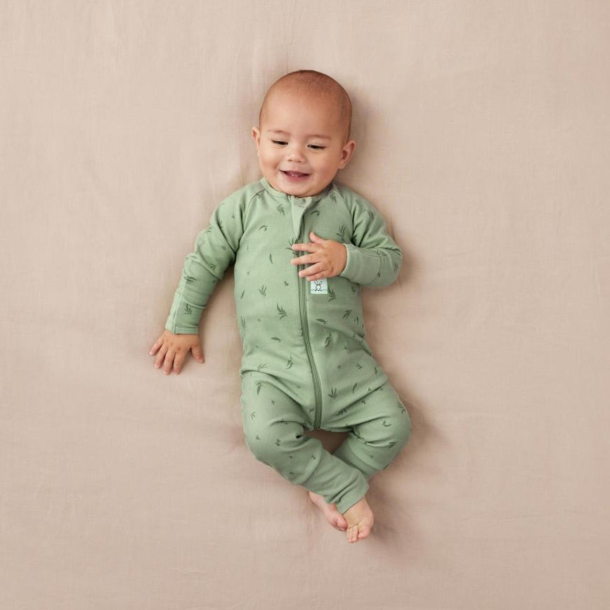 Baby wearing a green onesie on a beige background