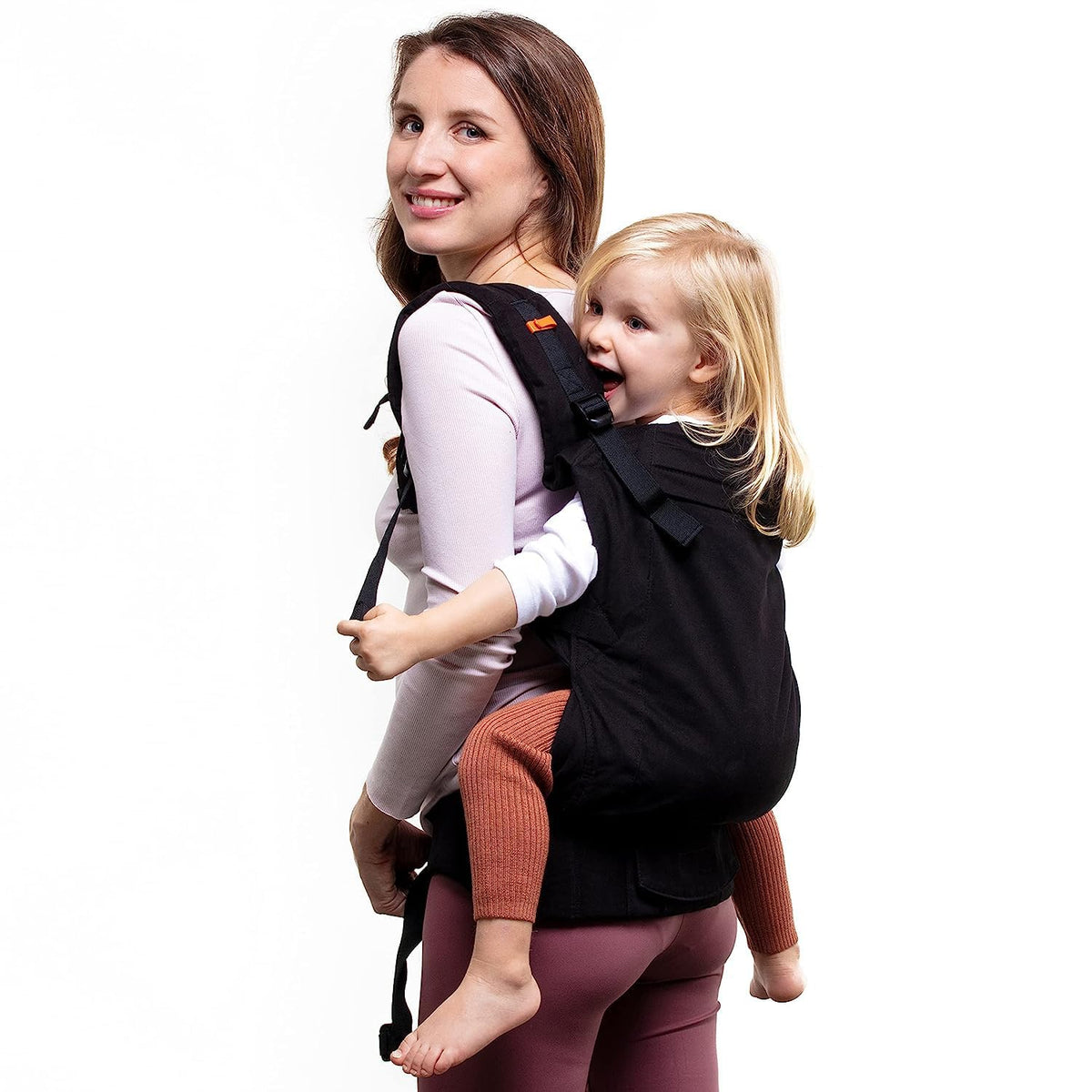 Woman carrying a 3 year old child in a black carrier against a white background